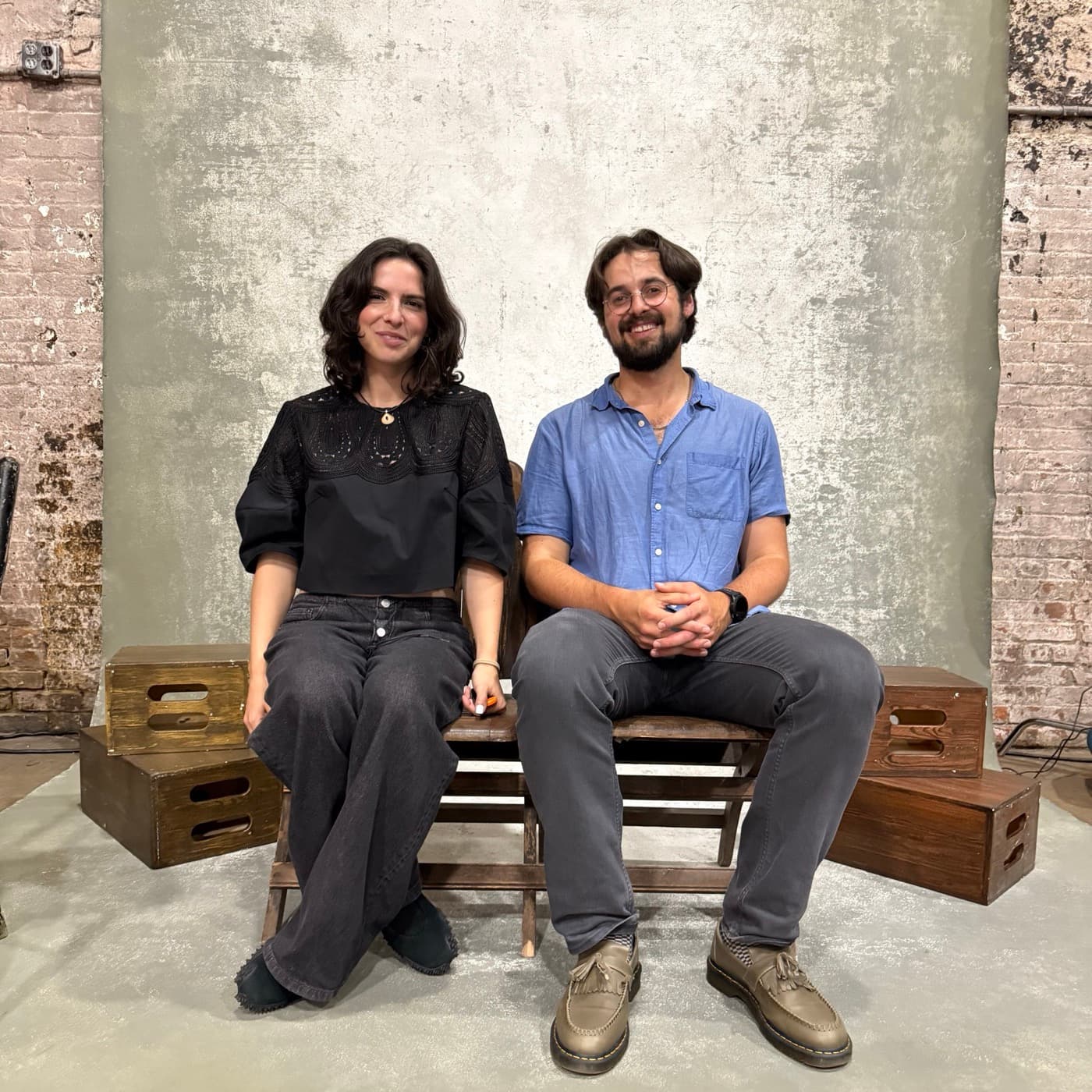 Emma Magidson and Jonah Bleckner seated on a bench in front of a canvas backdrop, apple boxes stacked either side