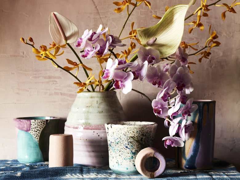 Still life of orchids, a speckled vase and pastel vessels on indigo linen, styled by Victoria Maiolo